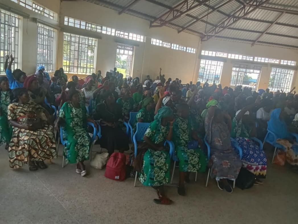Community women gathering in a large hall actively raising hands during the economic resilience training